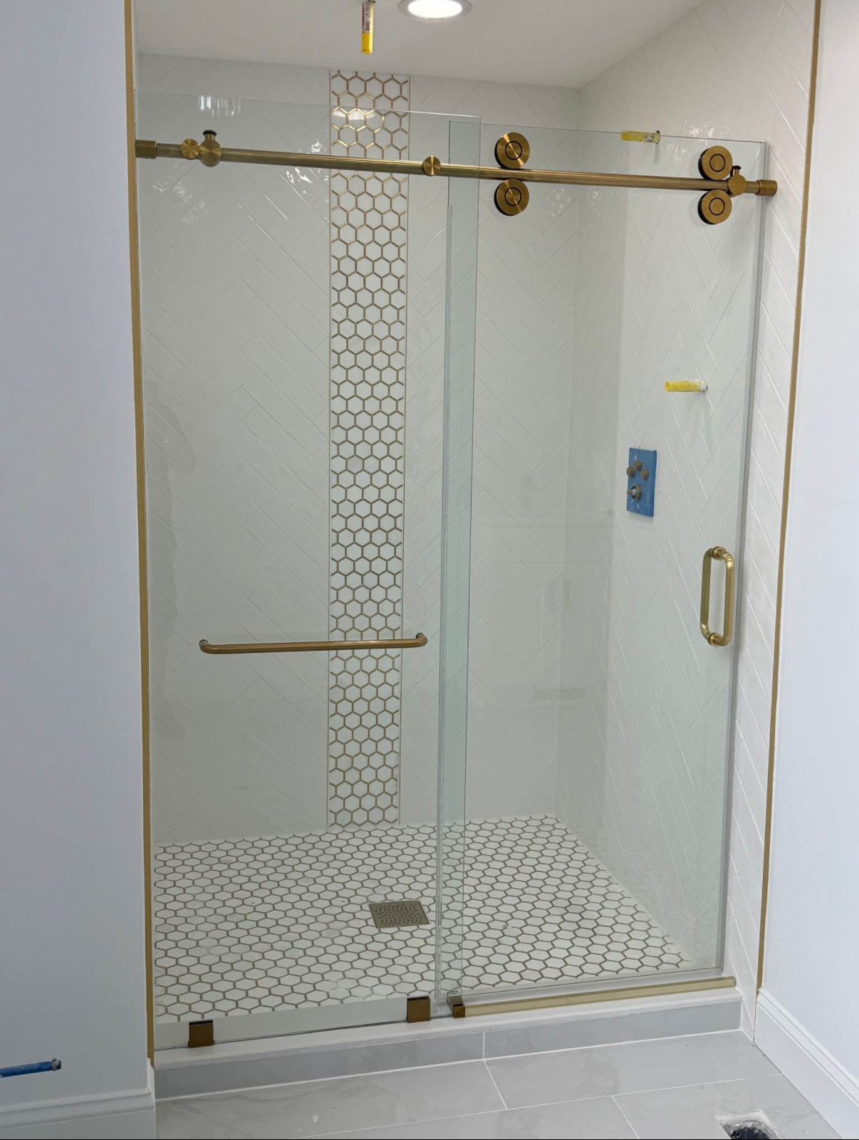 White herringbone tile shower with a gold hexagon mosaic accent stripe, mosaic pan and brushed gold sliding door