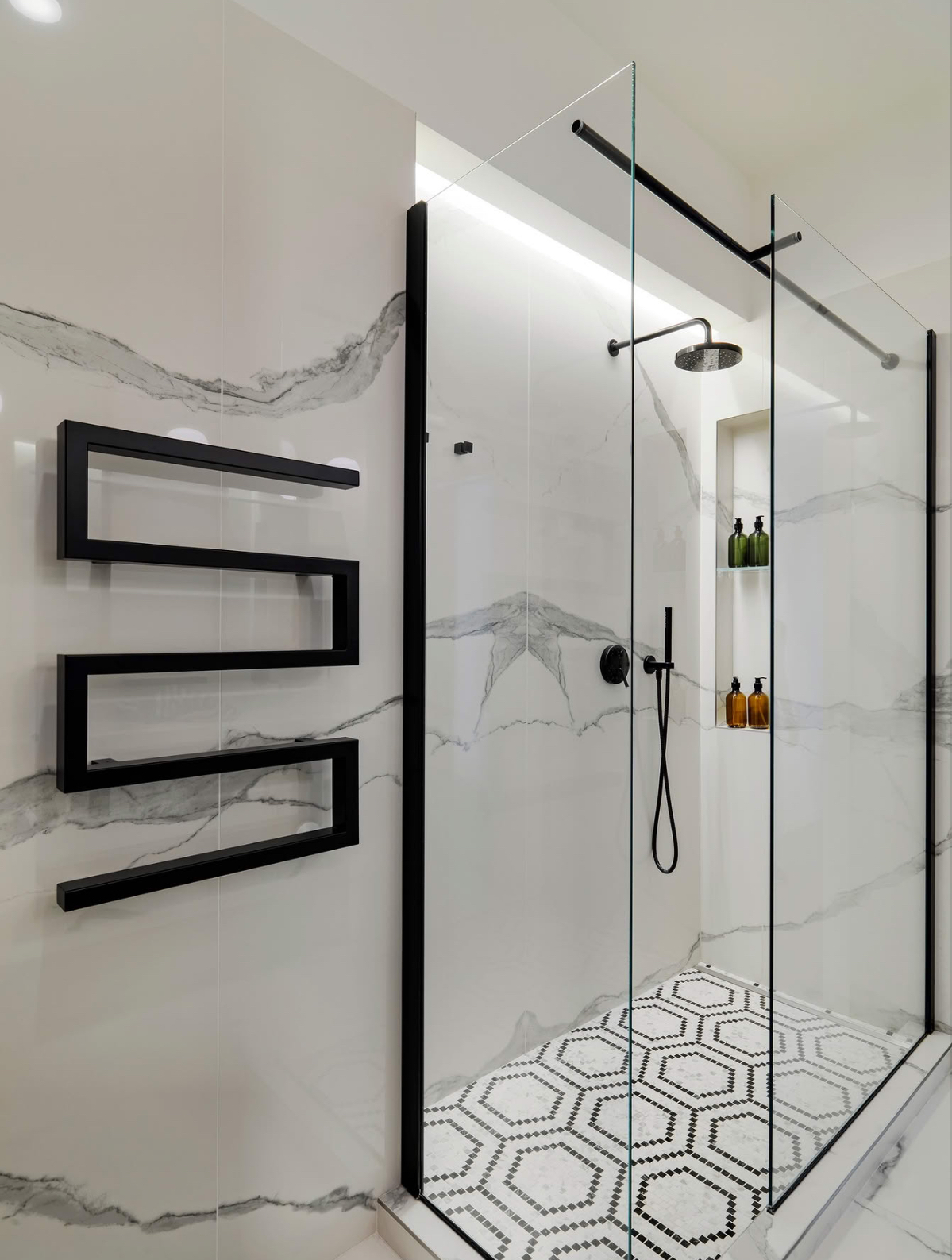 Statuario marble shower with a lit niche, black hardware and a hexagon marble mosaic shower pan