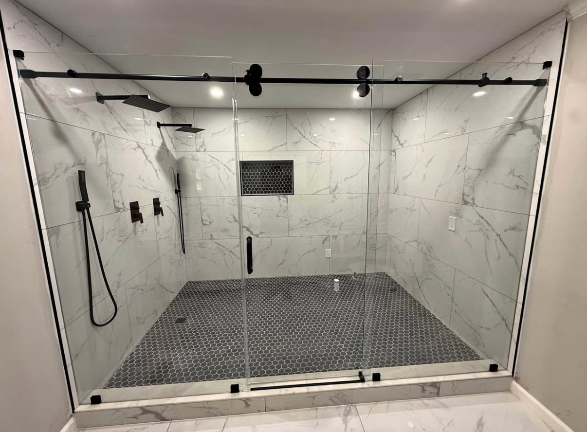 Wide double shower in large-format marble-look porcelain with black sliding glass doors and a grey hexagon mosaic pan