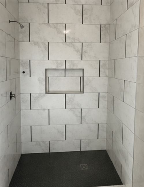 White marble subway tile shower with black shower floor and recessed niche