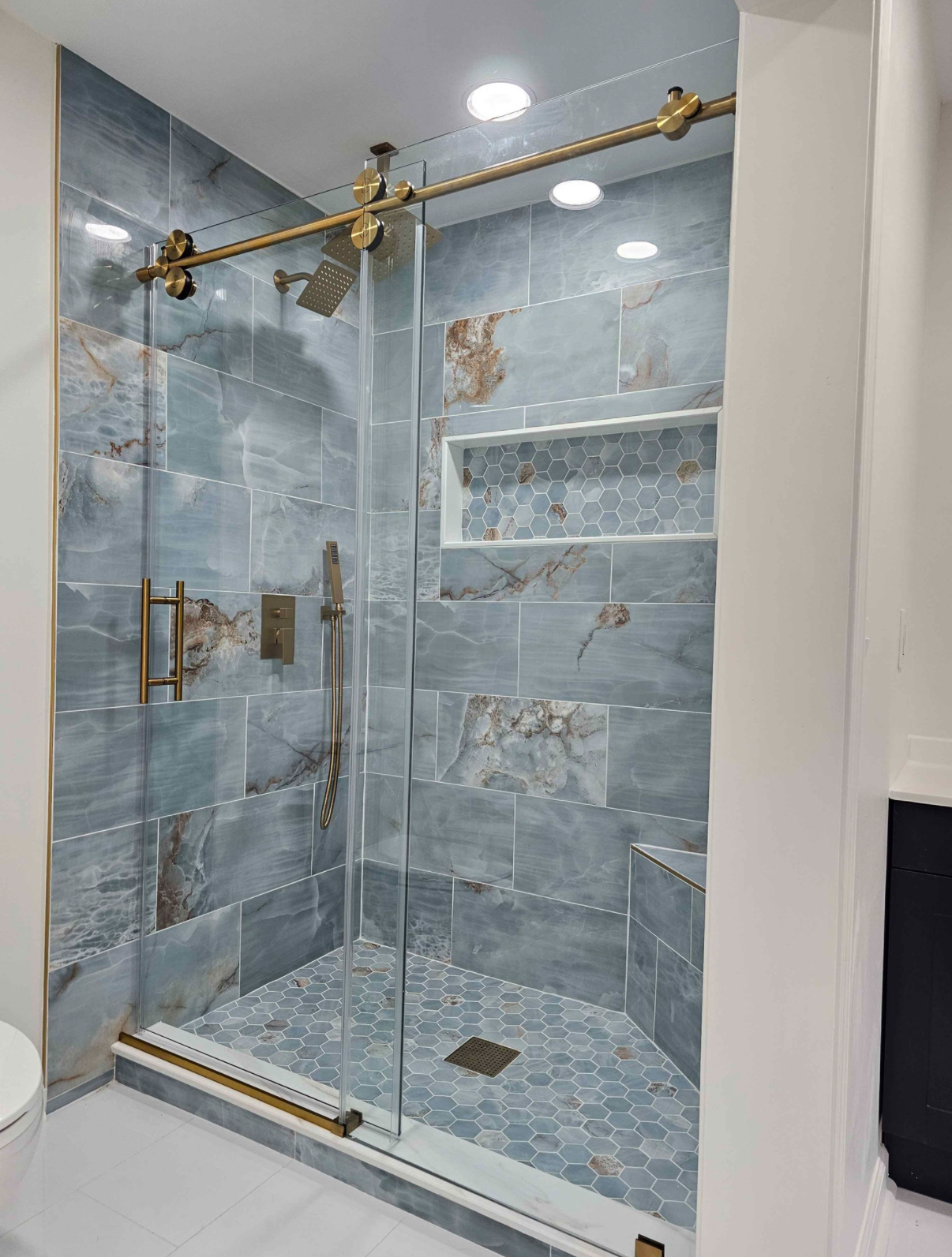 Blue onyx-look tile shower with brushed gold barn-style sliding glass door and hexagon mosaic niche and floor