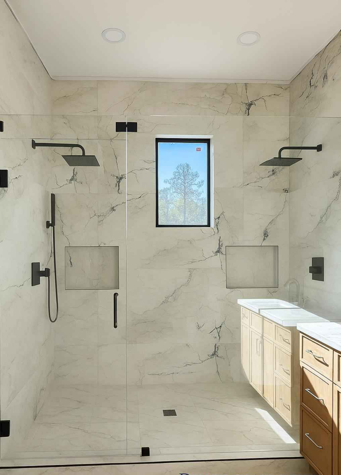 Double rain-head marble shower with frameless glass, twin niches and an oak double vanity alongside