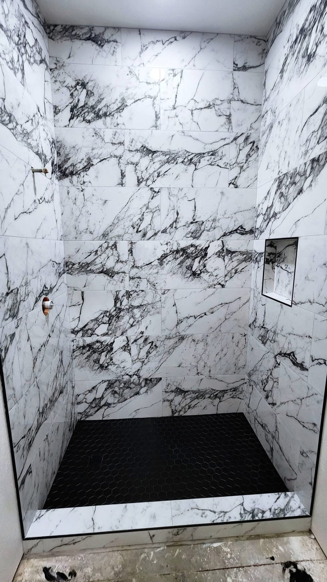 Walk-in shower clad in bold arabescato marble-look porcelain with a black hexagon mosaic pan and recessed niche